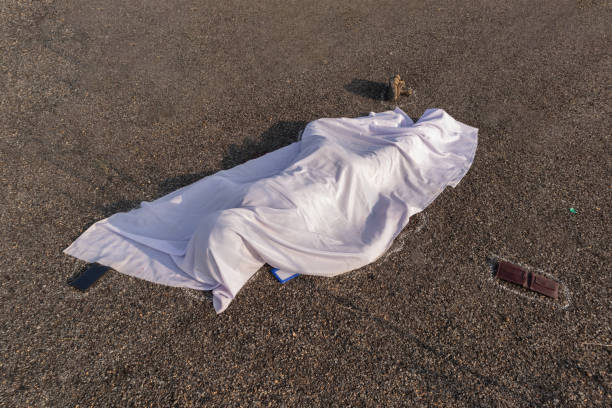 Concept of road accident scene, High angle view of chalk outlined dead body covered under white cloth laying on road